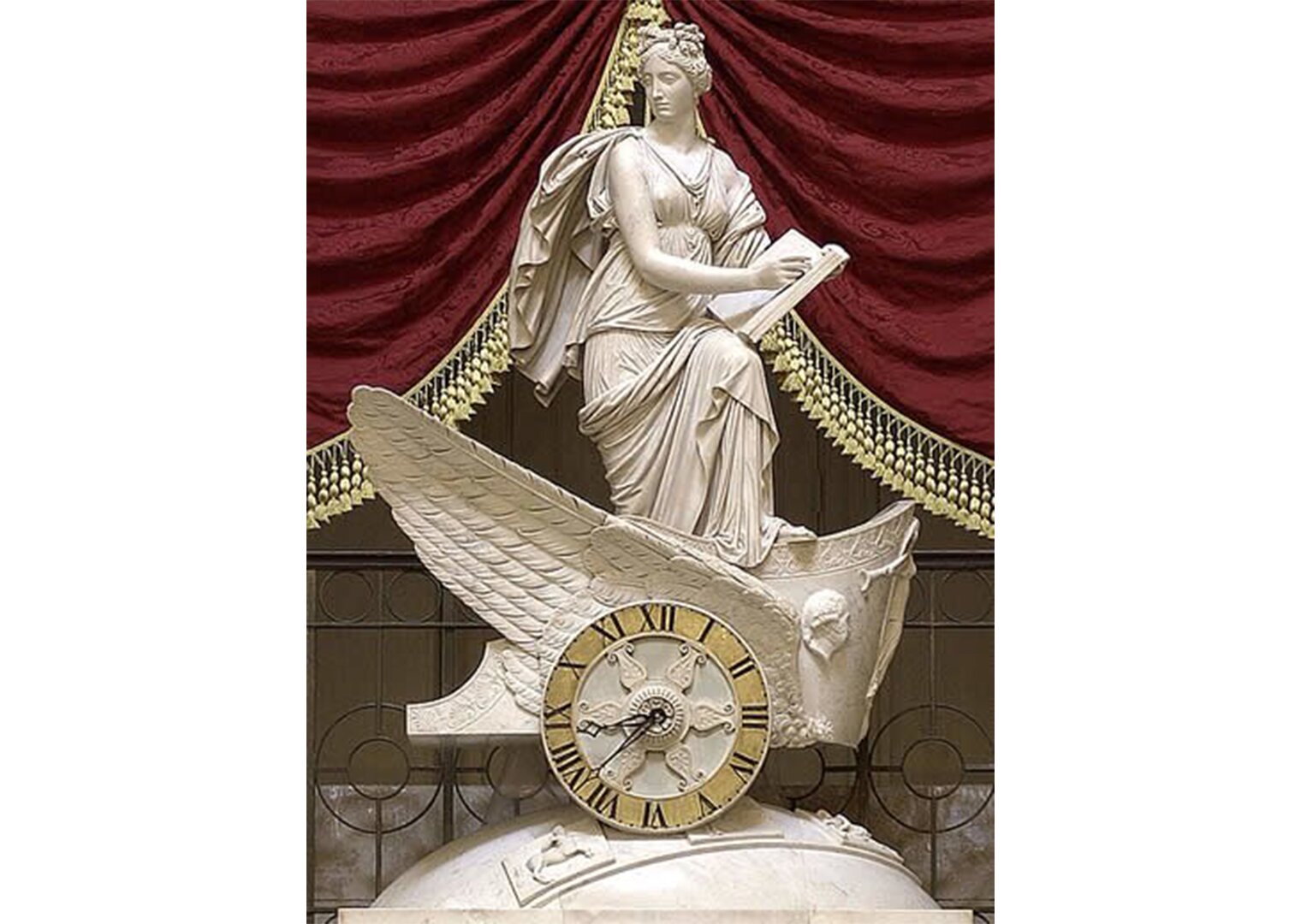 Na zdjęciu wykonany z marmuru posąg kobiety. Kobieta stoi, w dłoniach trzyma otwartą książkę. Stoi na skrzydłach, przed skrzydłami tarcza zegara.