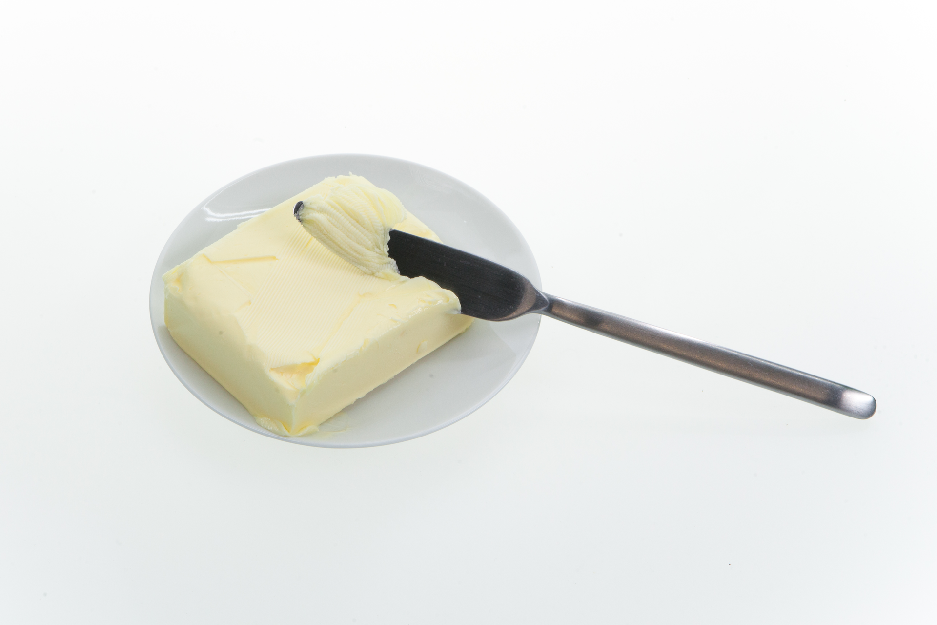 Zdjęcie przedstawia talerzyk z kostką masła i wbitym w nią metalowym nożem do smarowania. 