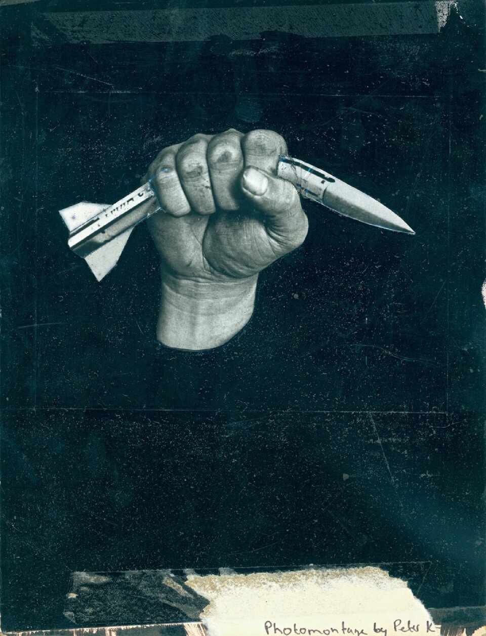 Ilustracja przedstawia ciemne, czarno‑turkusowe tło, na którym znajduje się ludzka dłoń zgniatająca w pół pocisk balistyczny. Tło jest porysowane, z widocznymi wytartymi fragmentami. Dłoń, ukazana pośrodku obrazu, jest jasna, ale na skórze oraz pod widocznym paznokciem kciuka można zauważyć zabrudzenia. Pocisk, dwukrotnie dłuższy od dłoni, zgina się pod jej naporem. 