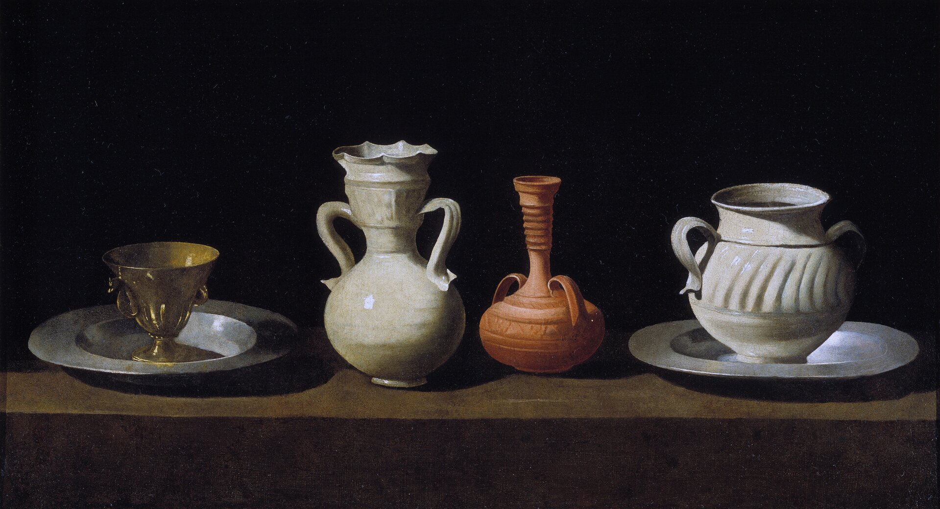 Ilustracja przedstawia obraz Francisco Zurbarána „Martwa natura z dzbanami ceramicznymi”. Ukazuje długi blat, na którym w rzędzie ustawione są naczynia. Od lewej strony stoją: złoty kielich na srebrnej podstawie, biały porcelanowy dzban, brązowy dzban z wąską, długą szyją i biały, pękaty dzban na srebrnej podstawie. Wszystkie naczynia są dekorowane, a te, które wykonane zostały z ceramiki, mają parę uszu. Światło pada z lewej strony i odbija się od naczyń, tworząc bliki. Tło martwej natury jest czarne i odcina się od naczyń.