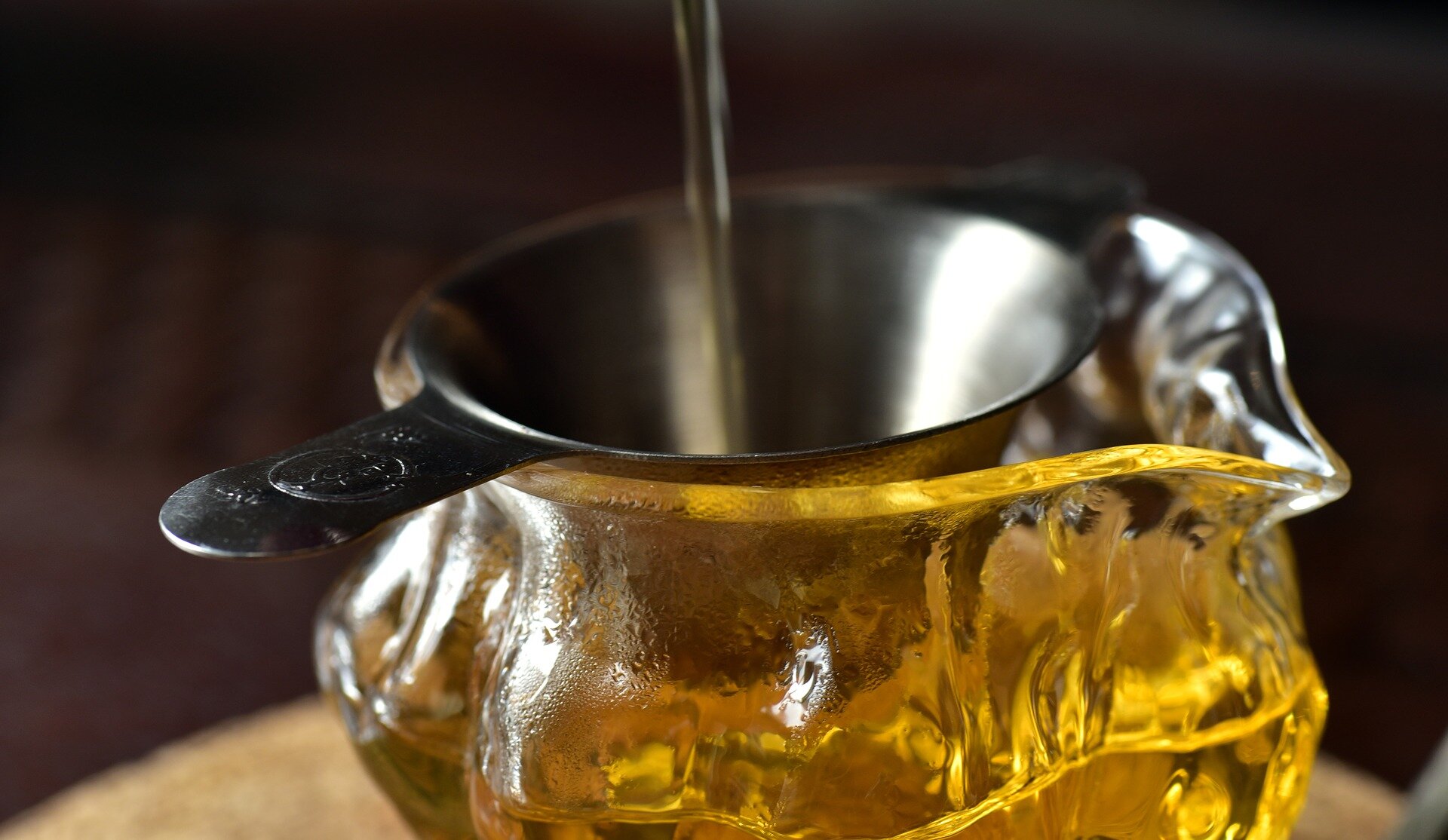 Zdjęcie przedstawiające mały metalowy lejek, przez który sączy się herbata do szklanego naczynia. 