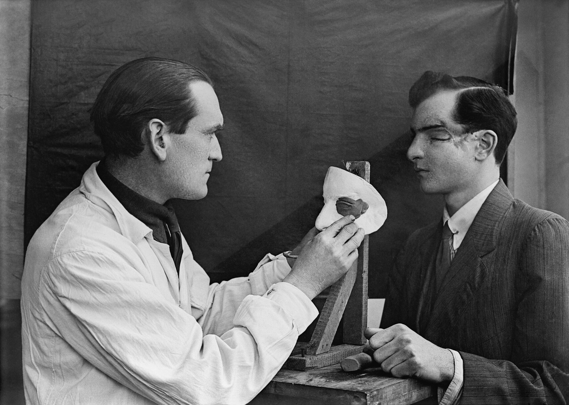 Fotografia czarno-biała przedstawiająca kapitana Francis Derwent Wood RA. który nakłada ostatnie szlify na talerz kosmetyczny wykonany dla brytyjskiego żołnierza z poważną raną na twarzy.