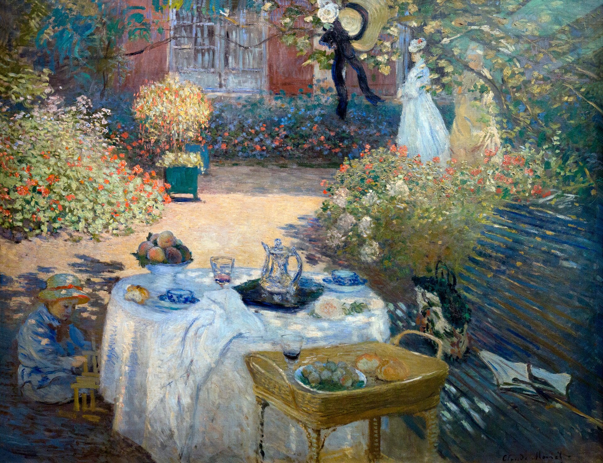Ilustracja przedstawia obraz „Śniadanie w ogrodzie” autorstwa Claude Moneta. Obraz ukazuje stół z obrusem znajdujący się w ogrodzie. Na stole znajdują się potrawy oraz napoje. Pod stołem widać dziecko bawiące się zabawkami.