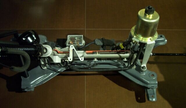 Ilustracja przedstawia elektrohydrauliczny system wspomagania kierownicy. W skład jego budowy wchodzi zespół pompy hydraulicznej, wspomagana przekładnia kierownicza, czujnik skrętu kierownicy oraz przewody hydrauliczne i elektryczne. Na zespół pompy hydraulicznej składają się: zbiornik oleju, silnik elektryczny, pompa, zawór bezpieczeństwa oraz sterownik.