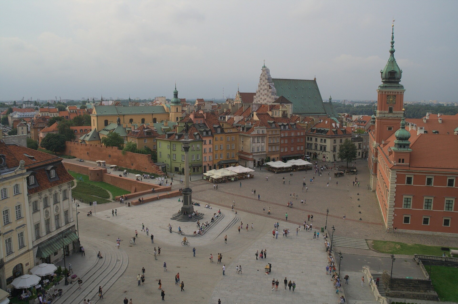 Ilustracja przedstawia zdjęcie z lotu ptaka na rynek miejski w Warszawie. Na środku widnieje kolumna Zygmunta. Ludzie spacerują po płycie rynku.  