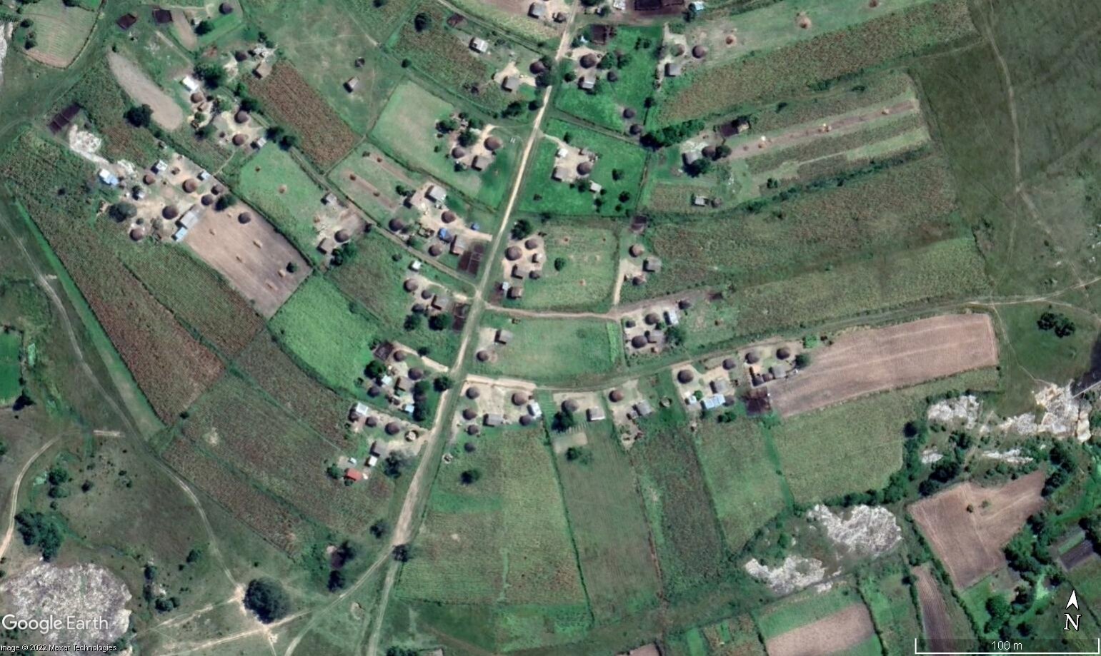 Ilustracja przedstawia domy i zabudowę gospodarczą w Zimbabwe. Gospodarstwa położone w korzystniejszych warunkach klimatycznych, są w stanie wyprodukować więcej żywności. Domy skupione są w okolicy drogi, za nimi rozciągają się pola uprawne.