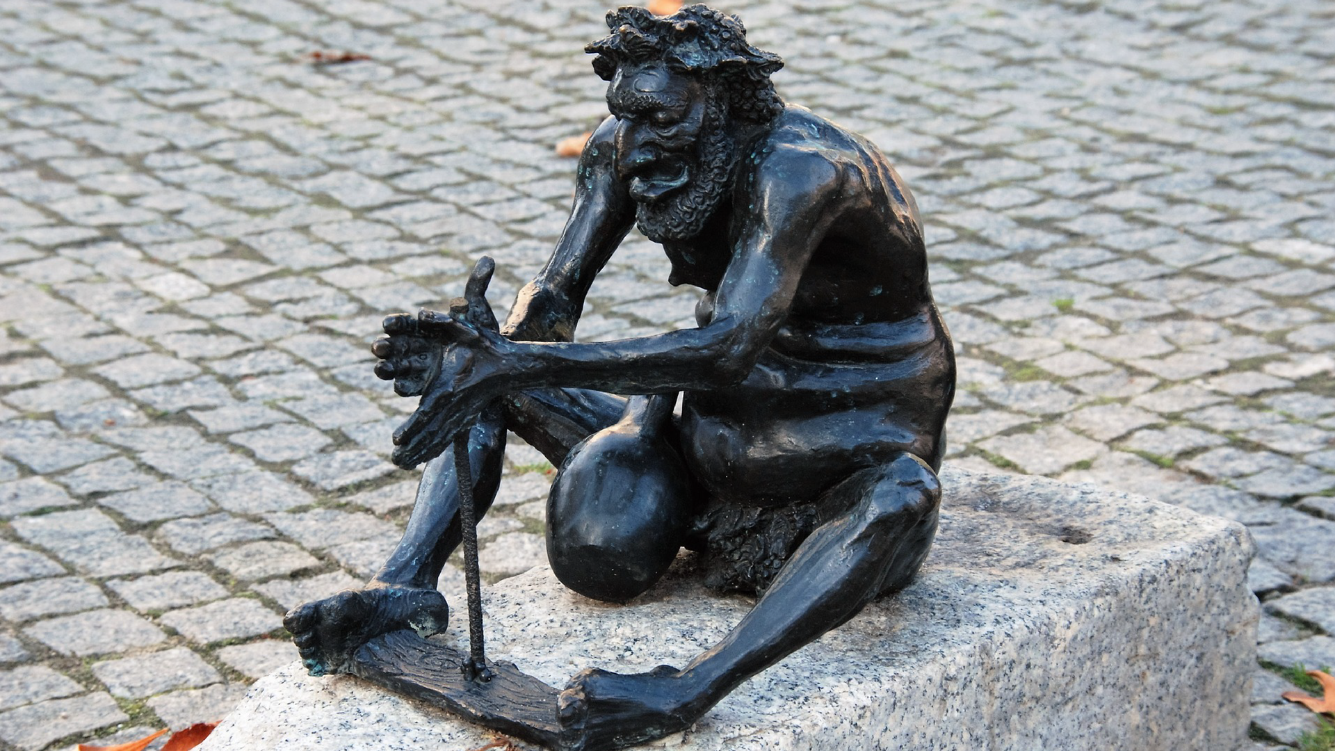 Zdjęcie przedstawia pomnik Bachusa, starożytnego boga płodności, dzikiej natury, winnej latorośli i wina. Postać przedstawiona jest jako dojrzały, brodaty mężczyzna z z nadwagą w pozycji siedzącej. Bachus próbuje rozpalić ogień kręcąc patykiem opartym o kawałek drzewa, który przytrzymuje stopami. O jego udo opiera się amfora służąca do przechowywania wina.