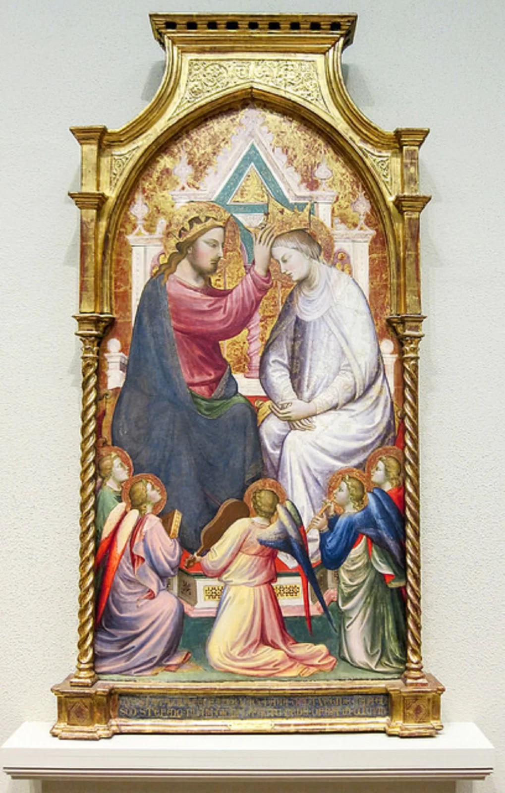Ilustracja przedstawia dzieło Mariotta di Narda, „Koronacja Najświętszej Maryi Panny z pięcioma muzykującymi aniołami”. Jest częścią nadstawy ołtarzowej. Obraz oprawiony jest w architektoniczną ramę z dwiema skręconymi kolumienkami oraz prosto zakończoną górną częścią, wypełnioną złotymi ornamentami. Ma kształt pionowego prostokąta, zamkniętego łukiem ostrym. Ukazuje scenę koronacji Marii. Na tronie siedzi Jezus i nakłada na głowę Matki koronę. Poniżej klęczy pięć aniołów, których głowy wzniesione są ku górze - patrzą na akt koronacji.