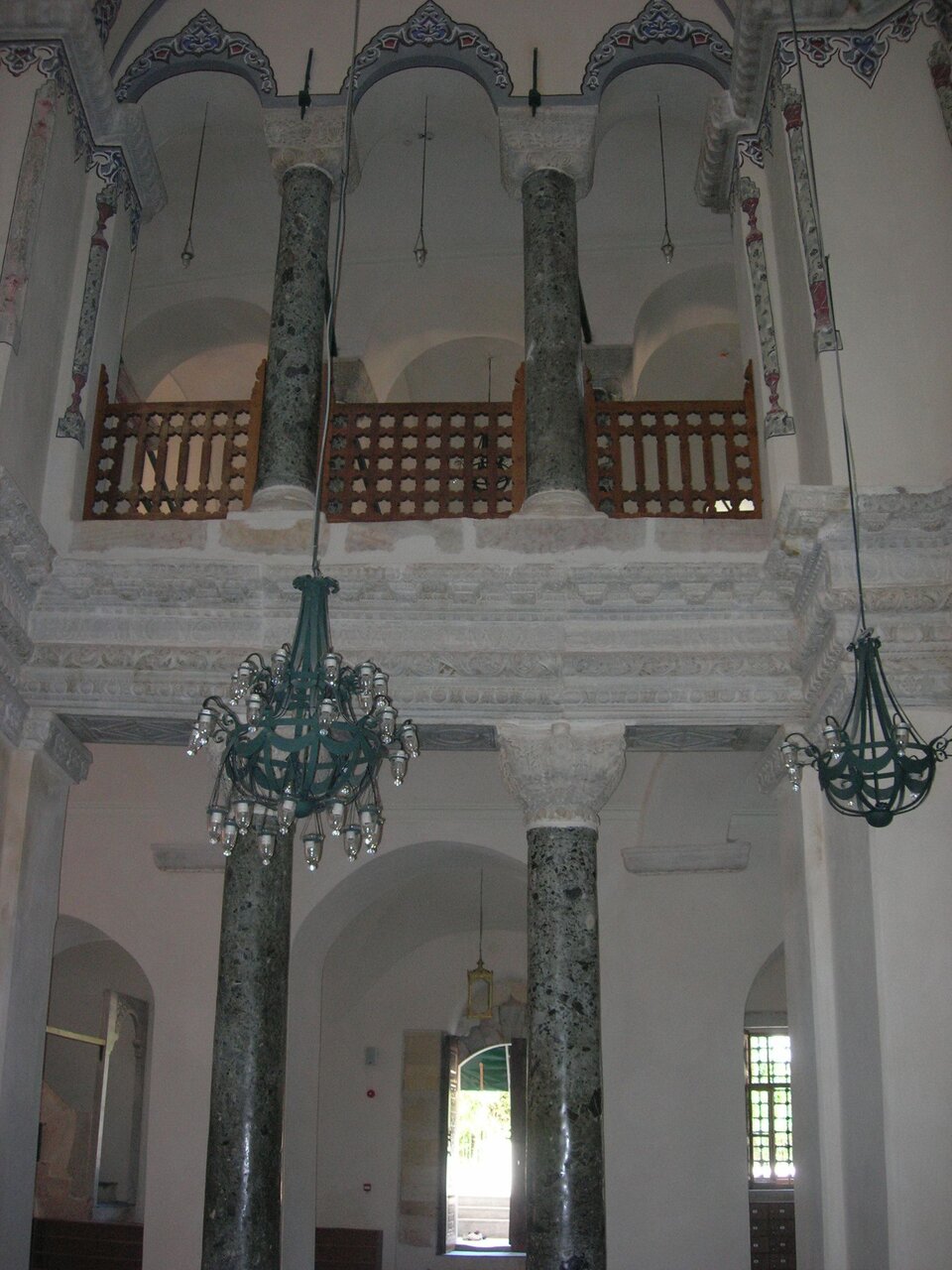 Fotografia przedstawia jedną z naw bocznych kościoła świętych Sergiusza i Bakchusa od wewnątrz. Sklepienia na poziomie parteru i o poziom wyżej są wsparte na szarych marmurowych kolumnach z głowicami koszowymi. Na pierwszym planie widoczne dwa ozdobne żyrandole wiszące na długich linach.