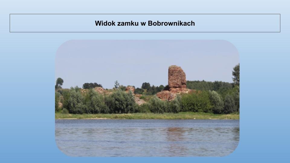 Niebieski slajd. U góry nagłówek: „Widok zamku w Bobrownikach”. Niżej zdjęcie przedstawiające ruiny zamku. Widoczny jest fragment muru i wieży z prawej strony. Zamek zbudowany jest z czerwonej cegły. Przed ruinami zielone drzewa, a dalej, u dołu zdjęcia, niebieska woda.