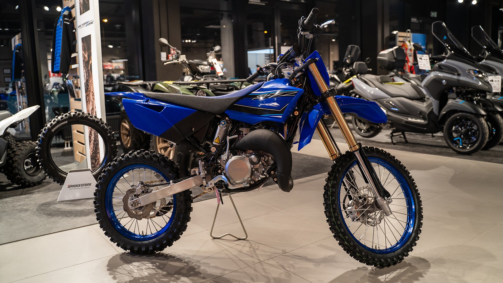 Zdjęcie przedstawia motocykl o lekkiej ramie. Motocykl jest wąski. Ma głęboki bieżnik na oponach. Pojazd ma niebieską ramę.  