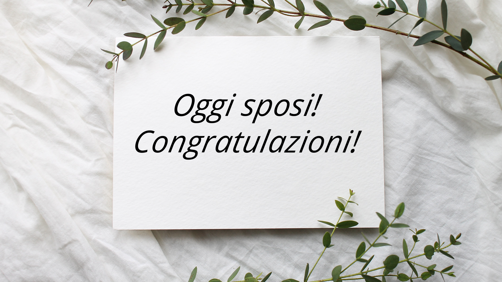 Zdjęcie przedstawia kartkę z życzeniami ślubnymi, obok kartki leżą gałązki. Tekst na kartce: "Oggi sposi! Congratulazioni!".