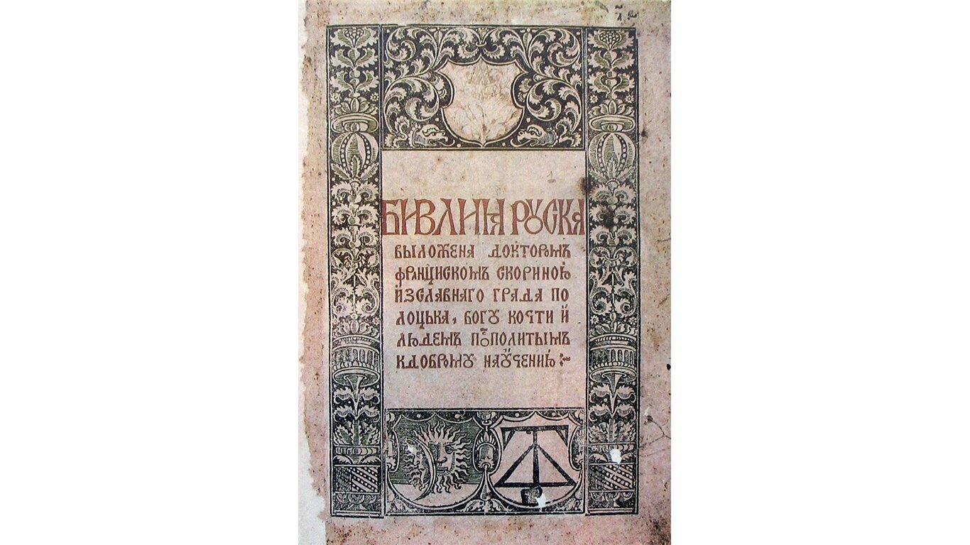 Fotografia przedstawia stronę z jednego z wydań Biblii. Litery zapisane są w cyrylicy, wokół nich umieszczono ramkę, która składa się z dekoracyjnych rycin. Dominują wzory kwiatowe, jednak na dole strony umieszczono tarcze herbowe. The photograph shows a page from one of the editions of the Bible. Letters are written in Cyrillic, a frame is placed around them, which consists of decorative engravings. Floral designs predominate, but at the bottom of the page there are coats of arms.