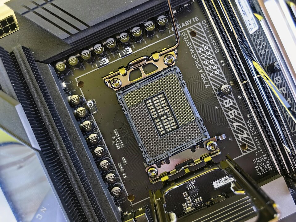Zbliżenie na płytę główną komputera typu GIGABYTE Z790 AORUS MASTER. Na środku znajduje się gniazdo procesora Intel LGA 1700 bez zamontowanego CPU. Wokół widoczne są elementy sekcji zasilania, sloty pamięci RAM DDR5 oraz metalowy mechanizm zabezpieczający procesor.