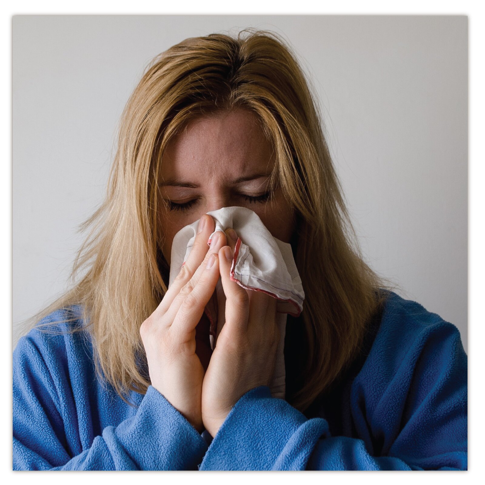 Na zdjęciu widoczna jest zakatarzona kobieta, która dmucha nos w chusteczkę.