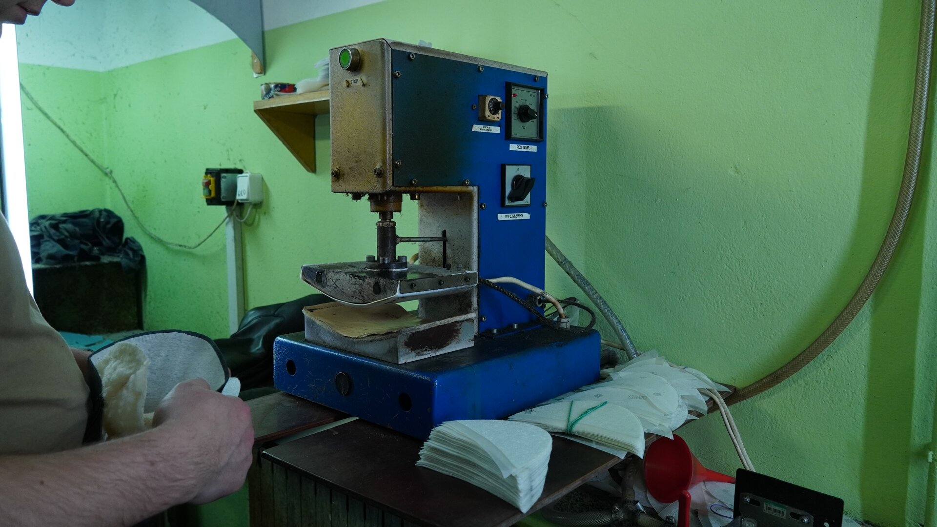 Zdjęcie przedstawia praskę do wklejania podnosków. Na pierwszym planie pracownik, który trzyma podnosek połączony z elementem cholewki. Nagranie tożsame z treścią.