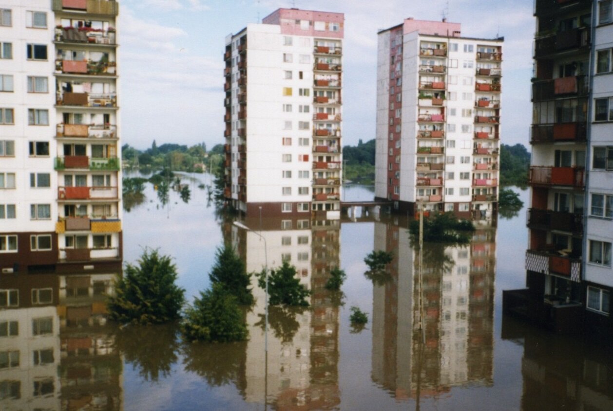 Zdjęcie przedstawia skutki powodzi w 1997 roku. Chodniki, trawniki i jezdnie przed czterema wieżowcami są zalane. Wszędzie wkoło nich stoi woda.