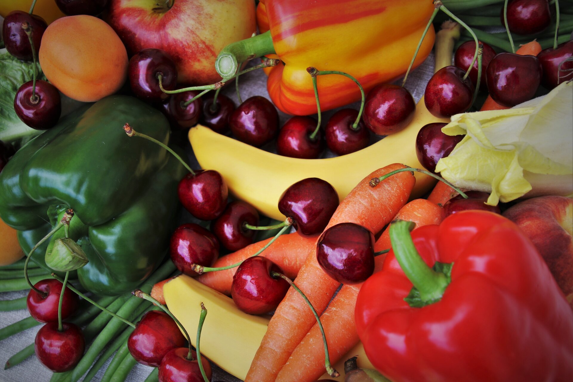 Zdjęcie przedstawia owoce i warzywa: zieloną i czerwoną paprykę, czereśnie, marchewkę, morele, banany, sałatę.
