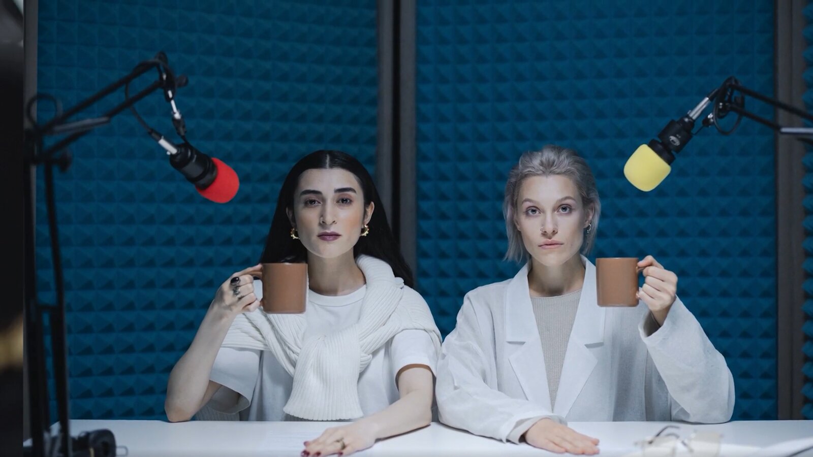   Ob deutschsprachige Nachrichten, Ratgeber oder auch Krimis – all das kannst du dir als kostenlose Podcasts unterwegs auf deinem Smartphone anhören und so dein Hörverständnis üben. Es gibt mittlerweile auch viele Lern‑Podcasts, mit denen du durch das Hören bzw. Wiederholen der gehörten Wörter oder Sätze deine Sprachkenntnisse verbesserst. Du musst Deutsch nicht unbedingt einwandfrei verstehen, um dir einen Podcast anhören zu können.
3. Deutschsprachige Podcasts hören
Ob deutschsprachige Nachrichten, Ratgeber oder auch Krimis – all das kannst du dir als kostenlose Podcasts unterwegs auf deinem Smartphone anhören und so dein Hörverständnis üben. Es gibt mittlerweile auch viele Lern‑Podcasts, mit denen du durch das Hören bzw. Wiederholen der gehörten Wörter oder Sätze deine Sprachkenntnisse verbesserst.
Opis: Ilustracja ukazuje studio nagraniowe, gdzie przed mikrofonami siedzą dwie młode kobiety, trzymając kubki w dłoniach.
