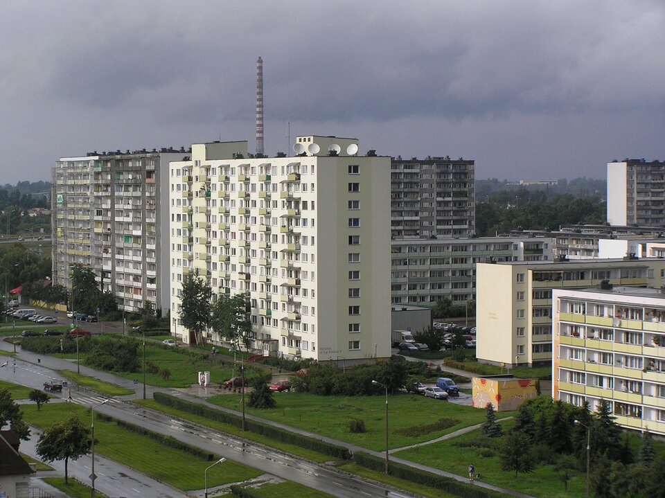 Zdjęcie ukazuje osiedle bloków. Bloki są kilkukondygnacyjne. Przed blokami są trawniki. 