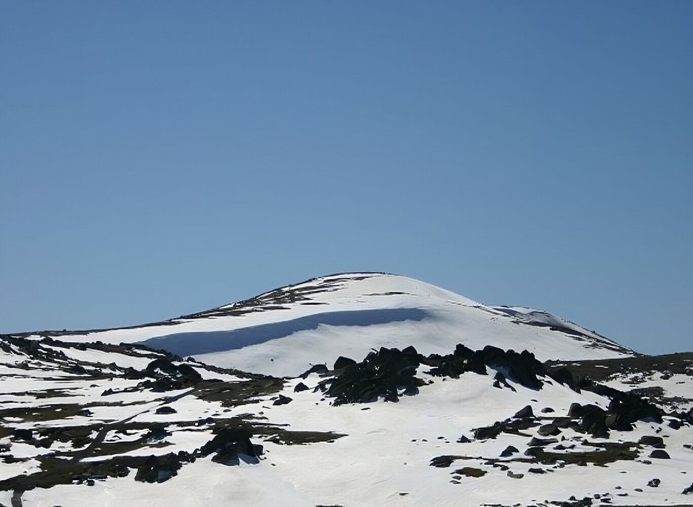 Na fotografii znajduje się ośnieżony szczyt górski na tle nieba. 