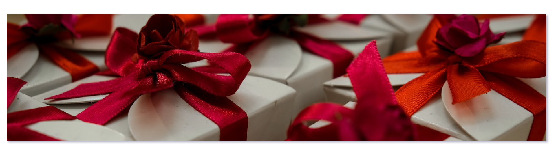 Zdjęcie przedstawia białe kartoniki prezentowe zawiązane czerwonymi wstążkami. 
