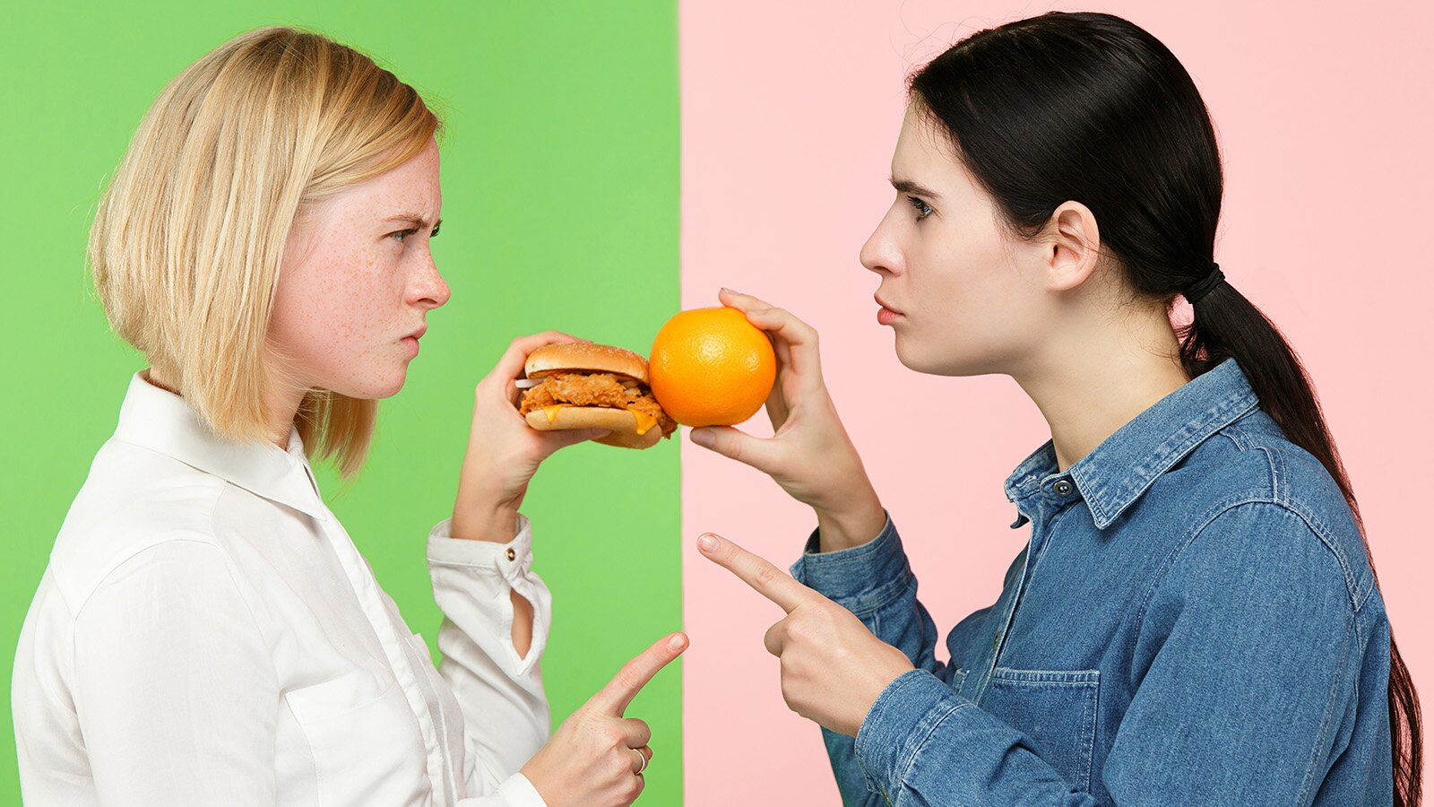 Zdjęcie przedstawia dwie nastolatki. Blondynka z lewej strony trzyma w lewej dłoni hamburgera oraz ma uniesiony palec wskazujący dłoni prawej. Na przeciwko niej stoi brunetka i trzyma w prawej dłoni owoc pomarańczy, jej palec wskazujący lewej dłoni też jest uniesiony. Dziewczyny patrzą sobie w oczy ze złymi minami.