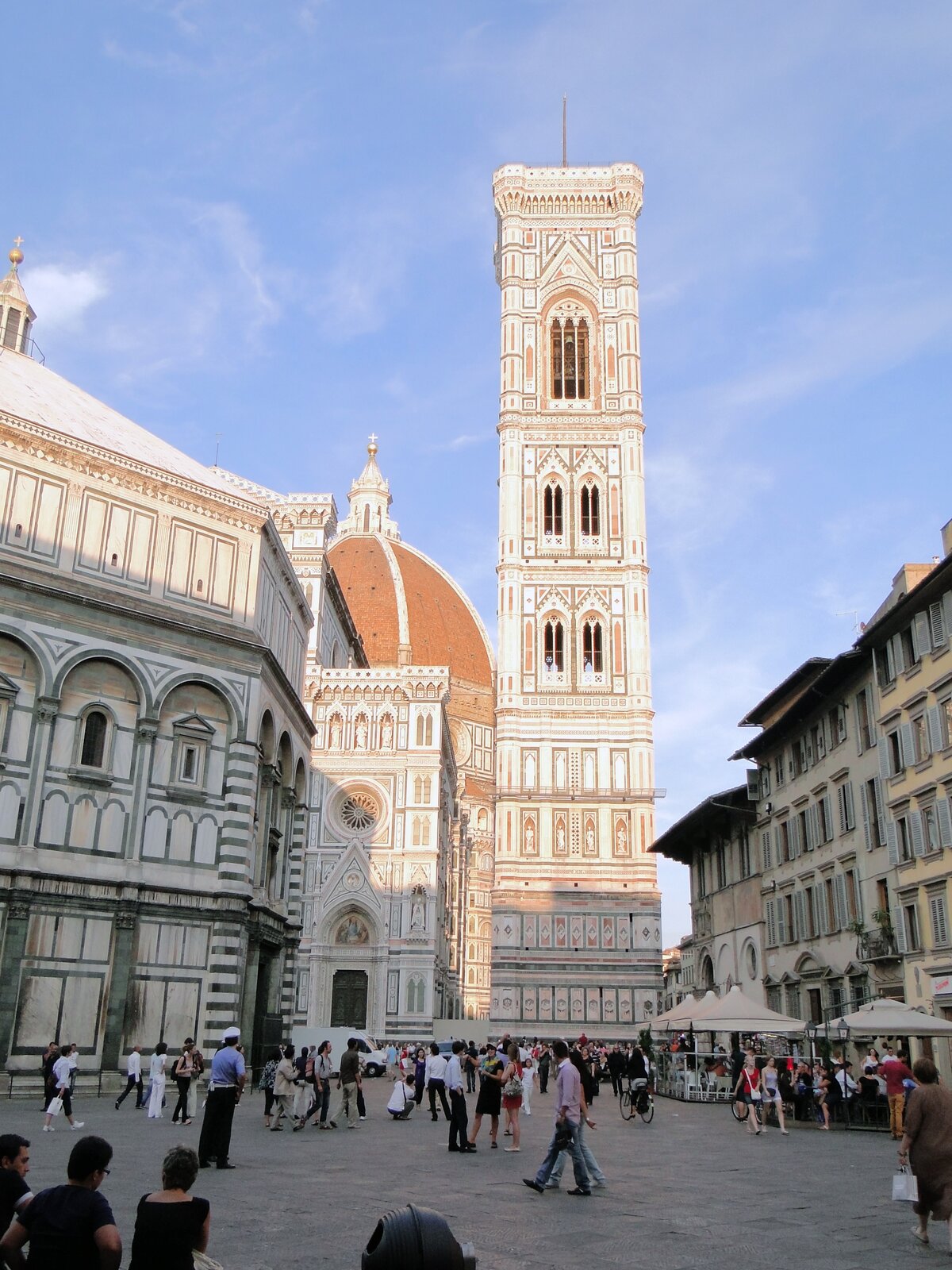 Ilustracja przedstawia dzwonnicę Giotta na placu we Florencji. Jest to wieża o kwadratowej podstawie z graniastymi wzmocnieniami w narożnikach. Elewacje zostały obłożone kolorowymi płytami marmuru o kolorze białym i różowym. Wieża posiada potrójne okno w najwyższej kondygnacji oraz dwie pary podwójnych okien w kondygnacjach niższych. Wszystkie okna są zakończone łukami ostrymi. Przed dzwonnicą znajduje się plac, przy którym ustawione są budowle. Za budynkami po lewej widoczny jest fragment kopuły i elewacji kościoła Santa Maria del Fiore. W tle rozciąga się niebieskie niebo.