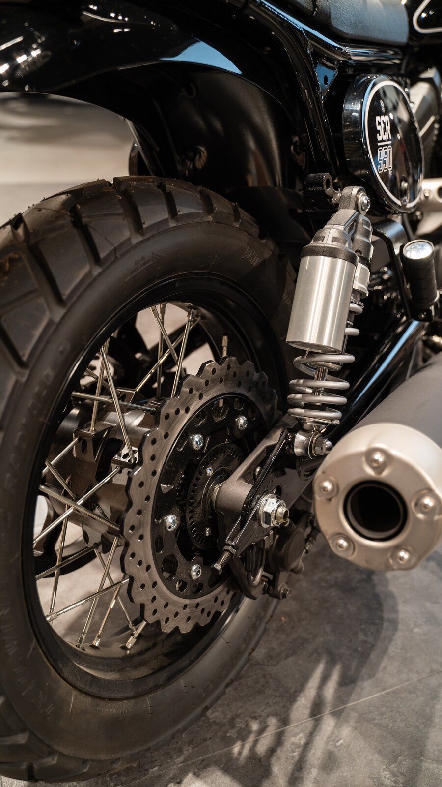 Na zdjęciu zbliżenie na koło motocykla. Pokazane są jego elementy z bliska. Koła są szprychowane.