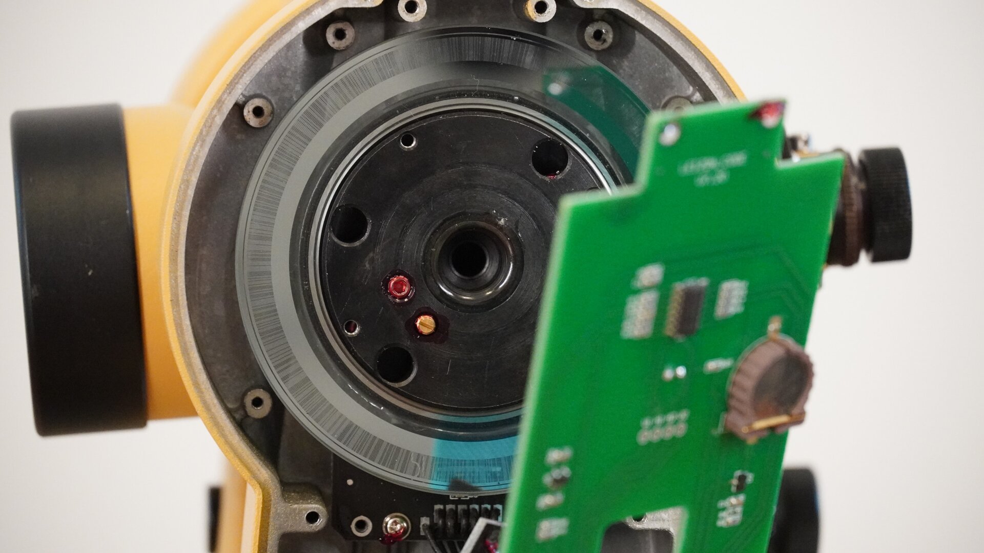 Na zdjęciu ukazano zbliżenie wnętrza teodolitu. Widać na nim mechanizm koła podziałowego pionowego odpowiedzialnego za odczyt kąta lunety. Na kole naniesione są kody paskowe odczytywane przez układy odczytowe umieszczone poniżej