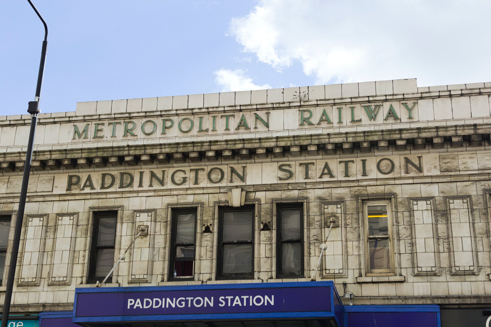 Zdjęcie przedstawia biały ceglany budynek, na którym umieszczono szyld "METROPOLITAN RAILWAY PADDINGTON STATION".