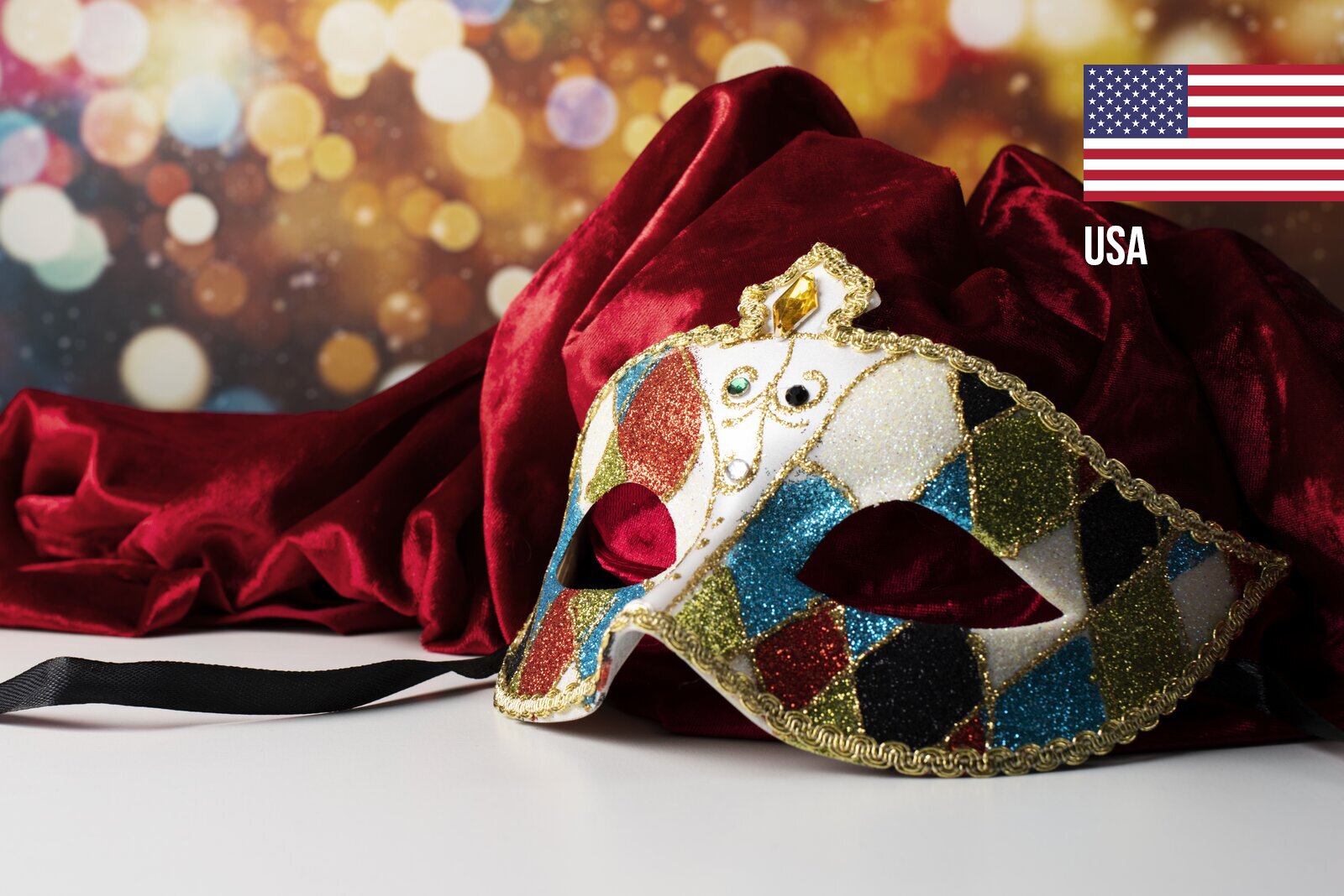 Na zdjęciu, po prawej stronie, na pierwszym planie, widoczna jest ozdobna, kolorowa maska na oczy. Maska ozdobiona jest brokatem w różnych kolorach (niebieskim, złotym i czerwonym) oraz złotą lamówką w formie plecionki. Po lewej stronie i za maską widoczny jest luźno ułożony bordowy materiał. W tle widoczne są świetliste kółka. W prawym górnym rogu widoczna jest flaga USA.
