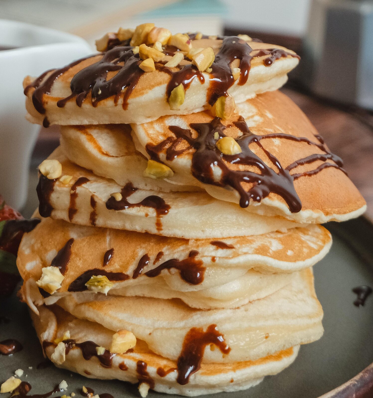 Zdjęcie przedstawia wieżę z małych puszystych naleśników polanych polewą czekoladową i posypanych kruszonymi orzechami.