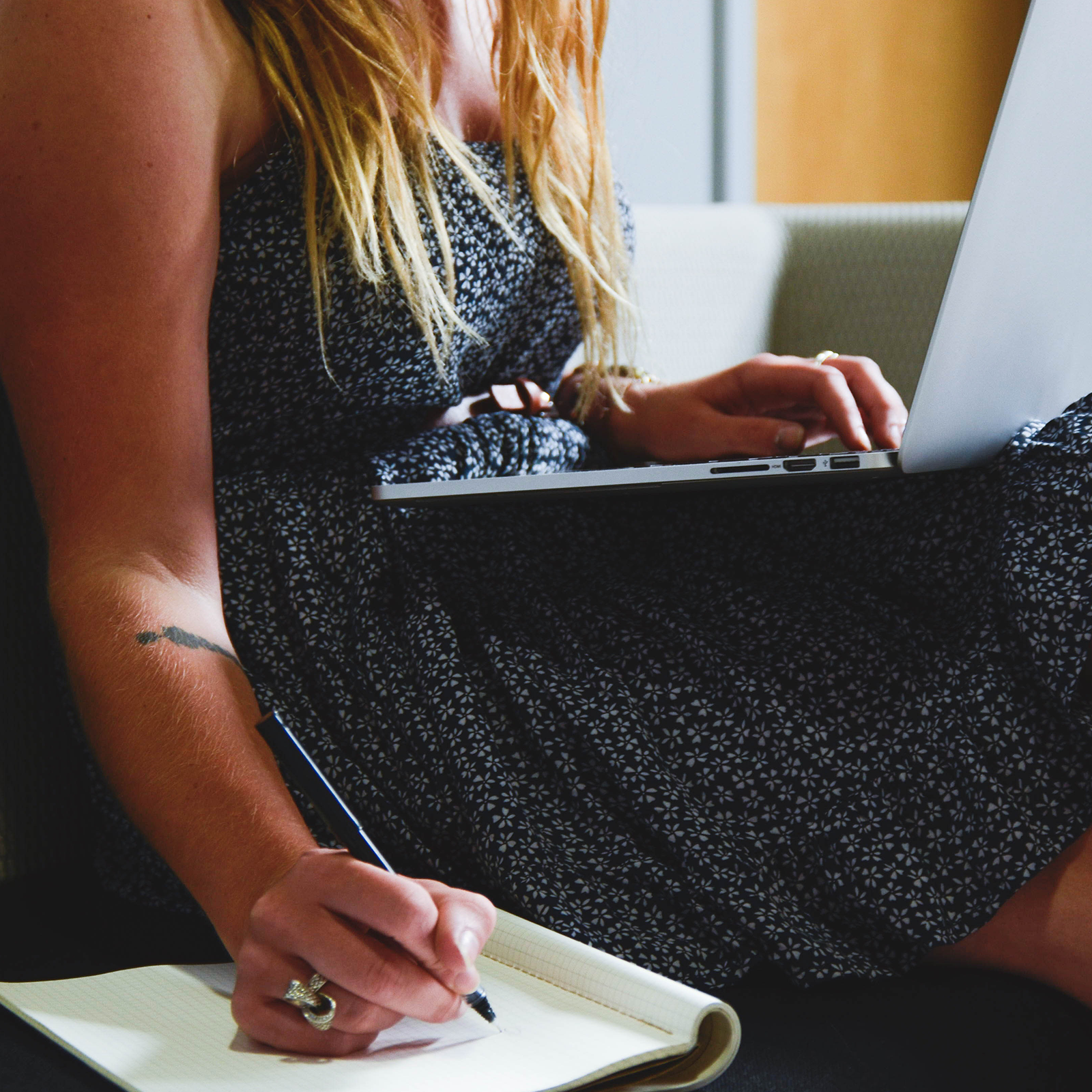 Zdjęcie przestawia dziewczynę siedzącą na kanapie. Na kolanach trzyma laptopa, z którego korzysta. Laptop nie ma podłączonej myszy ani żadnych innych sprzętów. Na kanapie leży zeszyt, w którym dziewczyna notuje coś długopisem. 