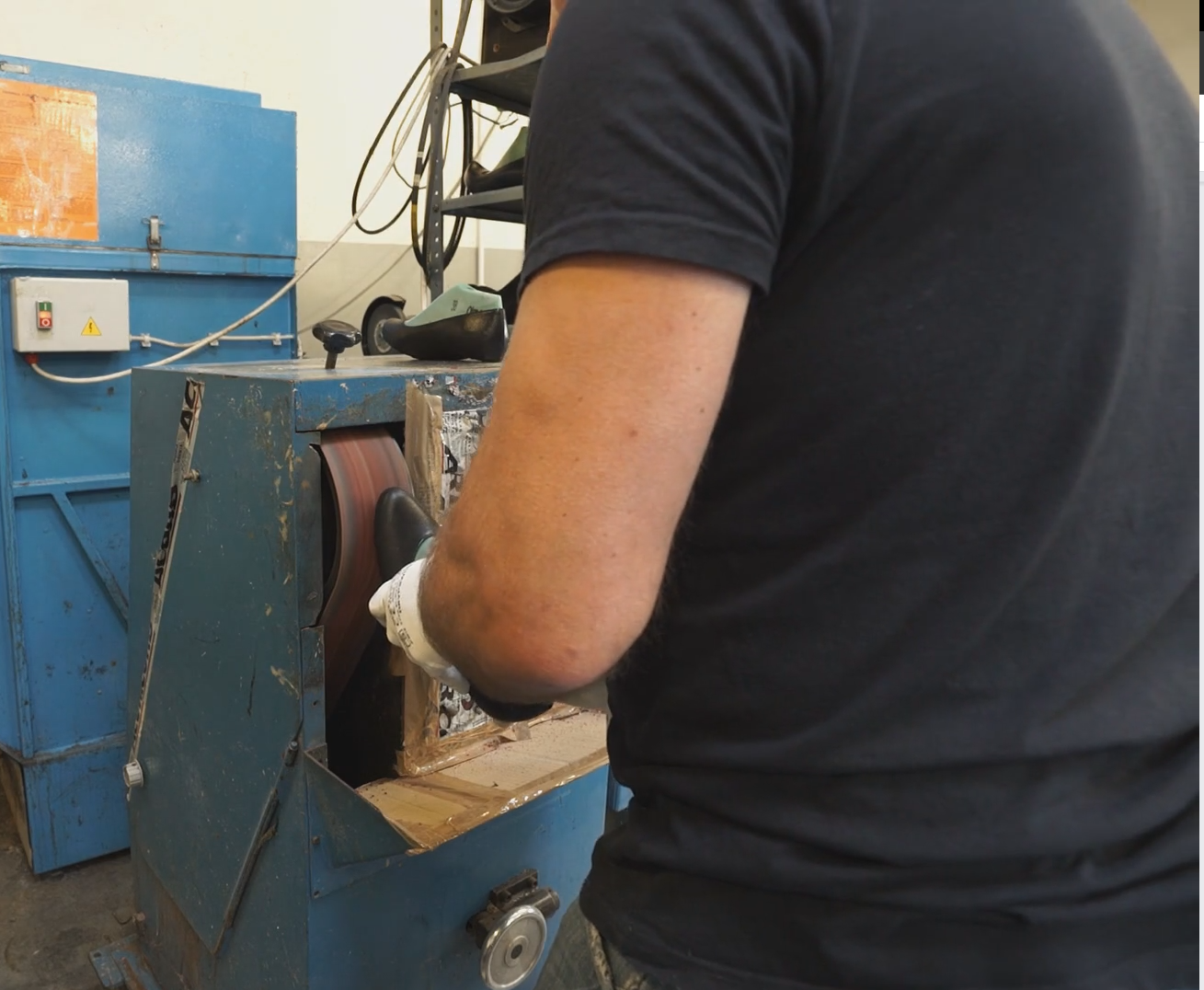 Na zdjęciu widoczny jest fragment mężczyzny, który trzyma w dłoni but i ściera jego spód na urządzeniu. Urządzenie to jest nieduże, ma niebieski kolor, z przodu ma obracającą się taśmę, na której ściera się obuwie. Nagranie tożsame z treścią.