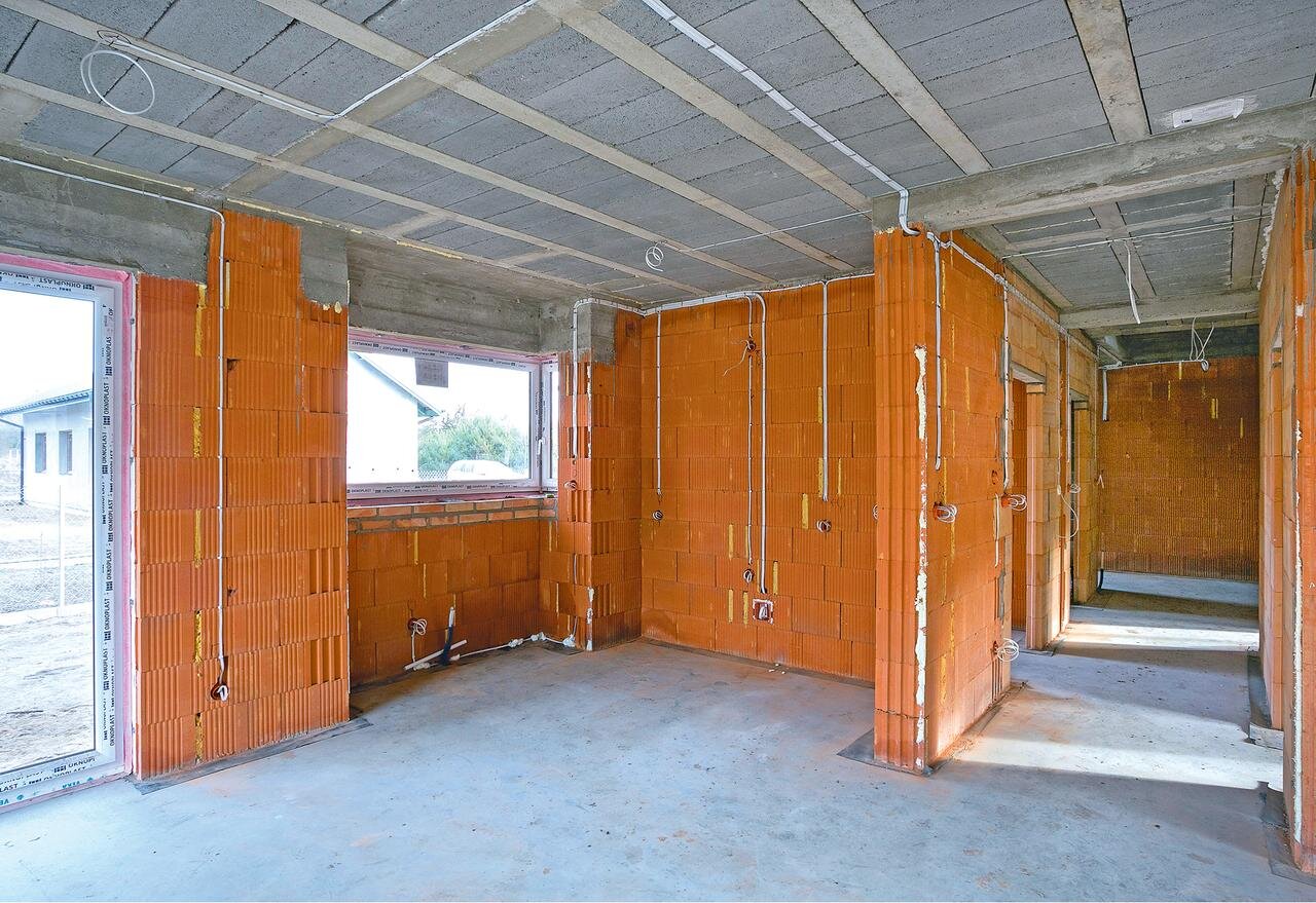 Na zdjęciu widoczne jest zdjęcie budynku w stanie surowym. Na ścianach i suficie rozprowadzono przewody instalacji elektrycznej oraz osadzono gniazdka elektryczne.