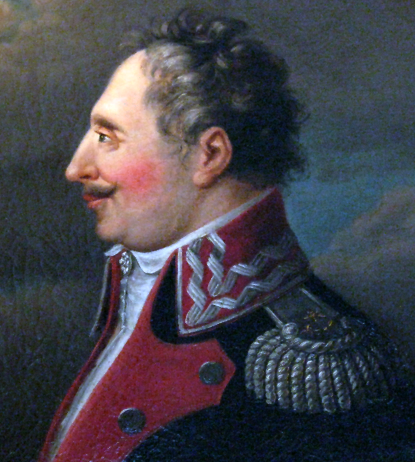 Na obrazie mężczyzna odwrócony bokiem. Ma ciemne i kręcone włosy, a w niektórych miejscach siwe. Pod nosem jest wąs. Ubrany jest w białą koszulę z wysoką, przylegającą do szyi, białą stójką, a także czarno‑czerwoną marynarką żołnierską. 