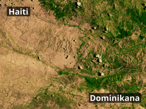Na zdjęciu satelitarnym fragment terenu. Z lewej strony odkryta gleba pozbawiona roślinności. Z prawej strony teren zalesiony. Granicę stanowi rzeka. Z lewej strony napis Haiti. Z prawej strony napis Dominikana. Zdjęcie pokazuje całkowitą deforestację terytorium Haiti w kontraście do zazielenionej Dominikany. 