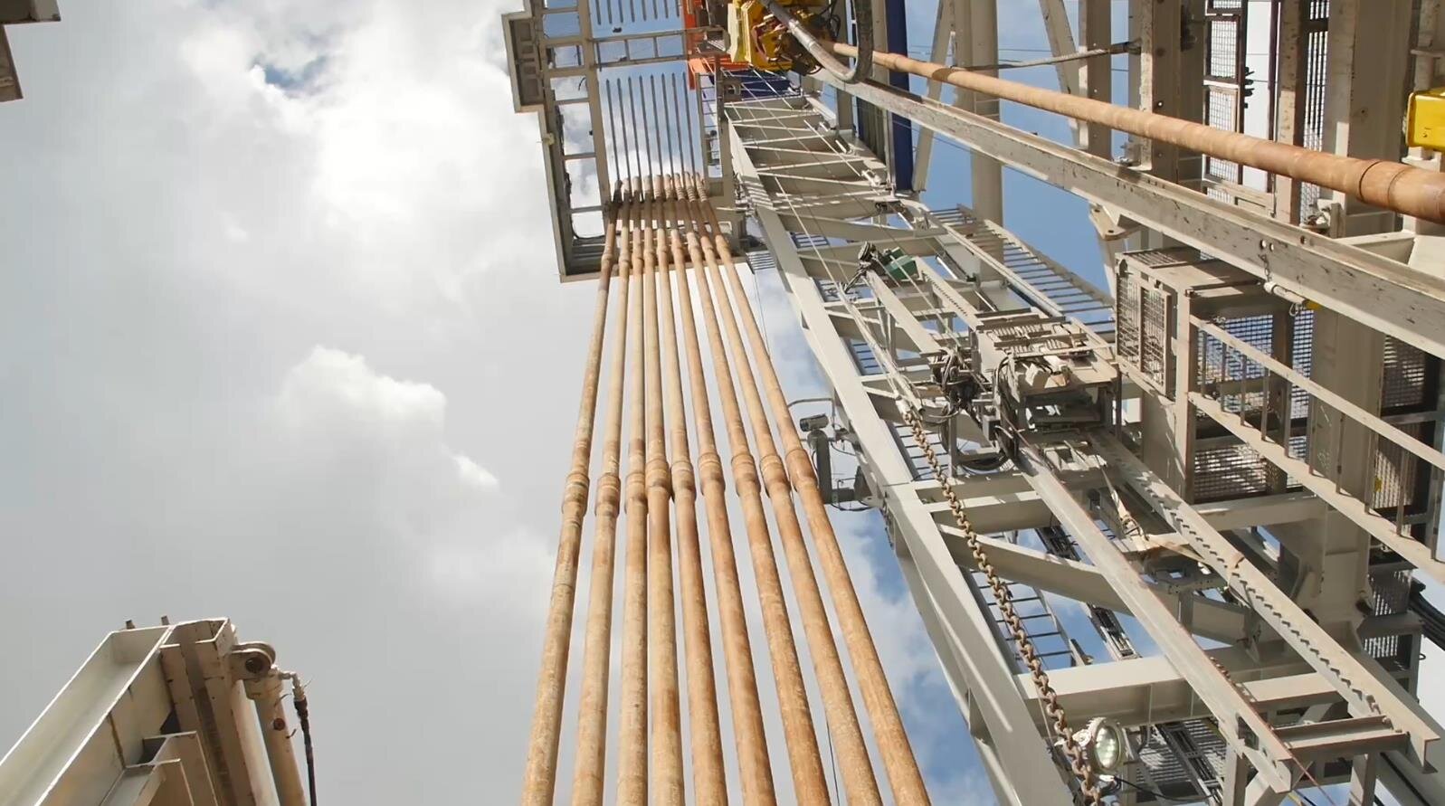 Na zdjęciu widoczny jest fragment wieżomasztu widoczny od dołu. W centralnej części zdjęcia znajduje się napęd Top Drive. Od dolnej części napędu odchodzi podłużna cylindryczna rura. Napęd znajduje się pomiędzy stalową konstrukcją kratową o kształcie podłużnego prostopadłościanu o orientacji pionowej. Po lewej stronie napędu widocznych jest dziesięć rur. Rury są magazynowanie równolegle względem siebie i względem wieży.