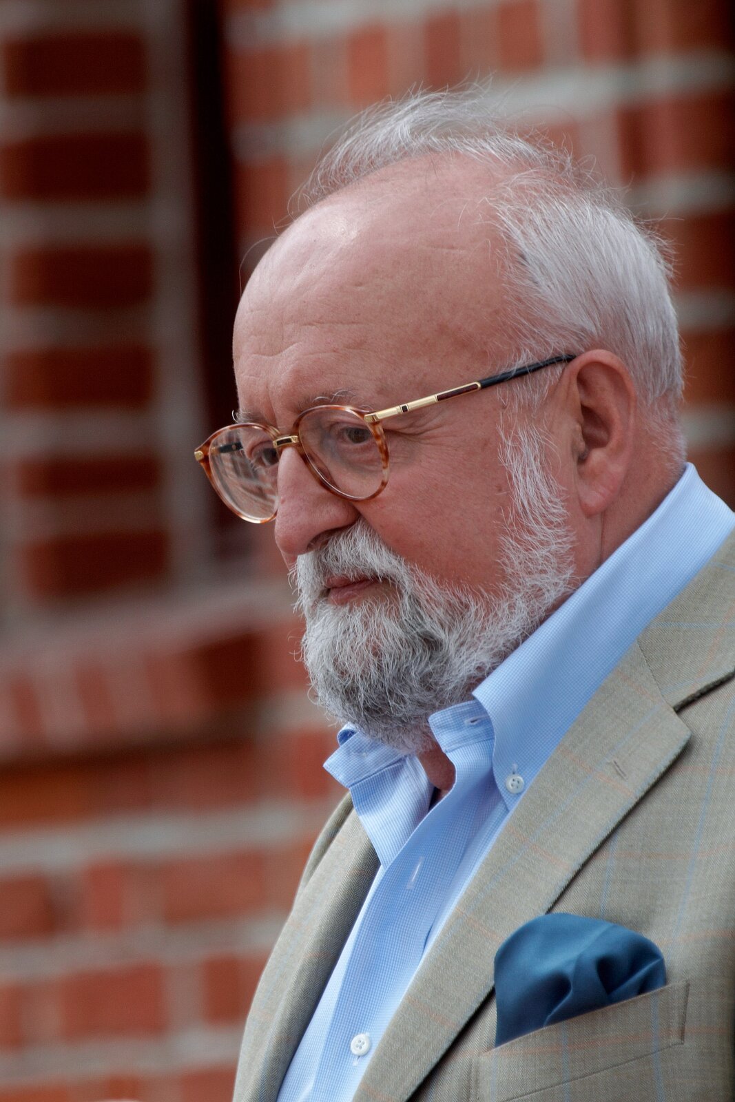 Ilustracja przedstawia: Krzysztof Penderecki w 2008 roku. Na fotografi widać starszego mężczyznę w szarej marynarce z granatową poszetką i jasnoniebieskiej koszuli. Mężczyzna ma okulary, siwy zarost i włosy.