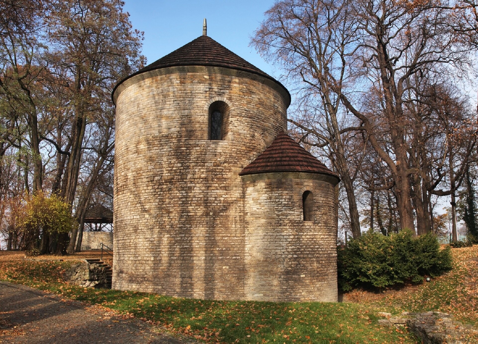 Ilustracja przedstawia kaplicę św. Mikołaja, w Cieszynie. Zbudowana jest z płaskich ciosów wapiennych na planie koła z apsydą. Kryta jest dachem stożkowym. W murach znajdują się małe okna z glifem, czyli głęboko osadzone i rozszerzające się na zewnątrz. Rotunda położona jest na terenie parku.