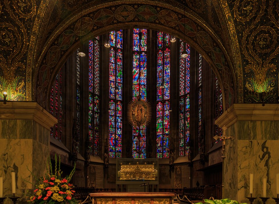 Ilustracja przedstawia masywne arkady zdobione złotą politurą, zwieńczone wydatnym gzymsem. Za nimi witrażowe okno, na którym widnieje postać Matki Boskiej z dzieciątkiem otoczona promieniami. Pod wizerunkiem Matki Boskiej złota szkatuła.