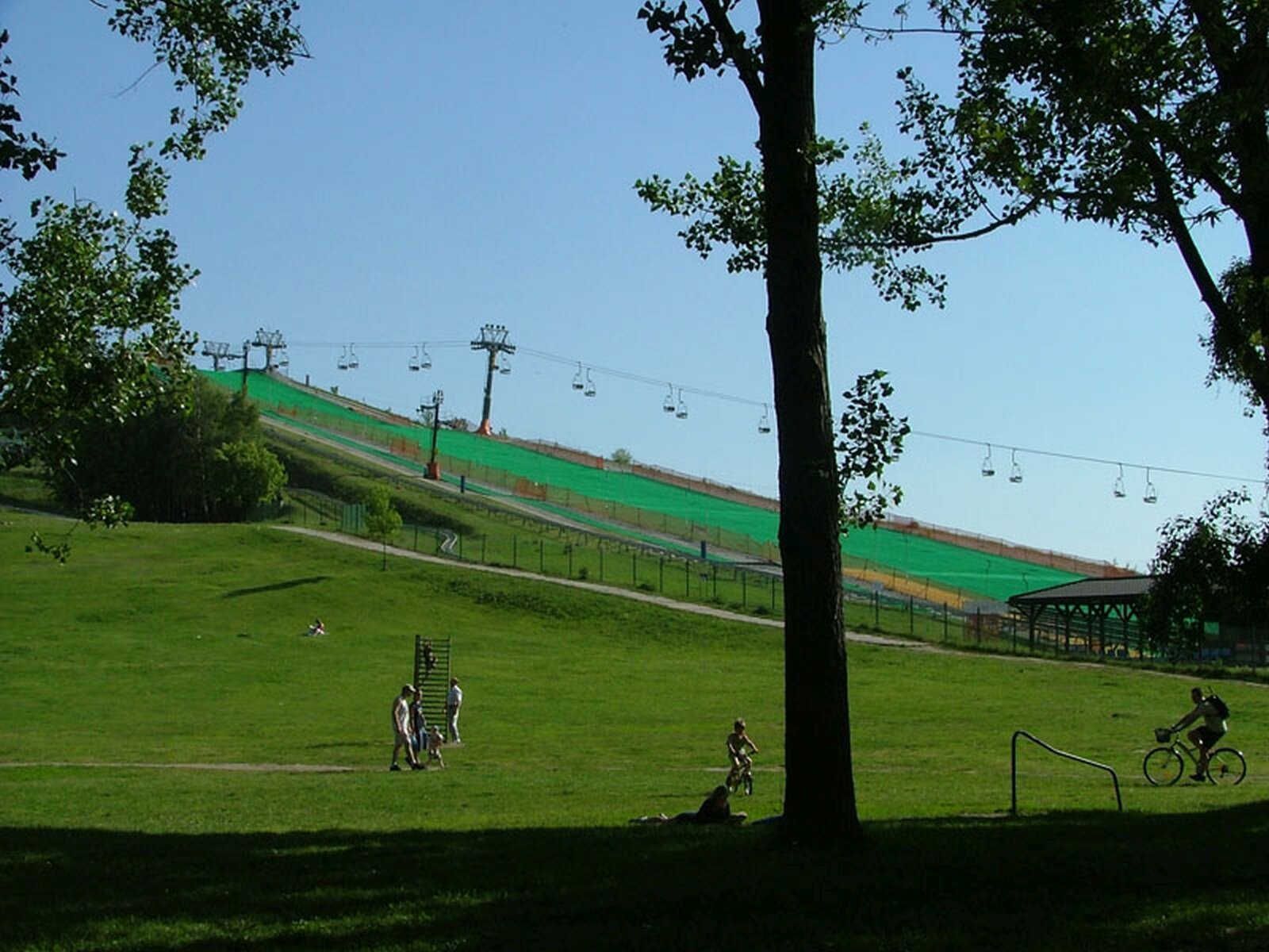 Zdjęcie przedstawia park. Na pierwszym planie łąka. Obok znajduje się wyciąg krzesełkowy. Wszędzie rośnie zielona trawa. 