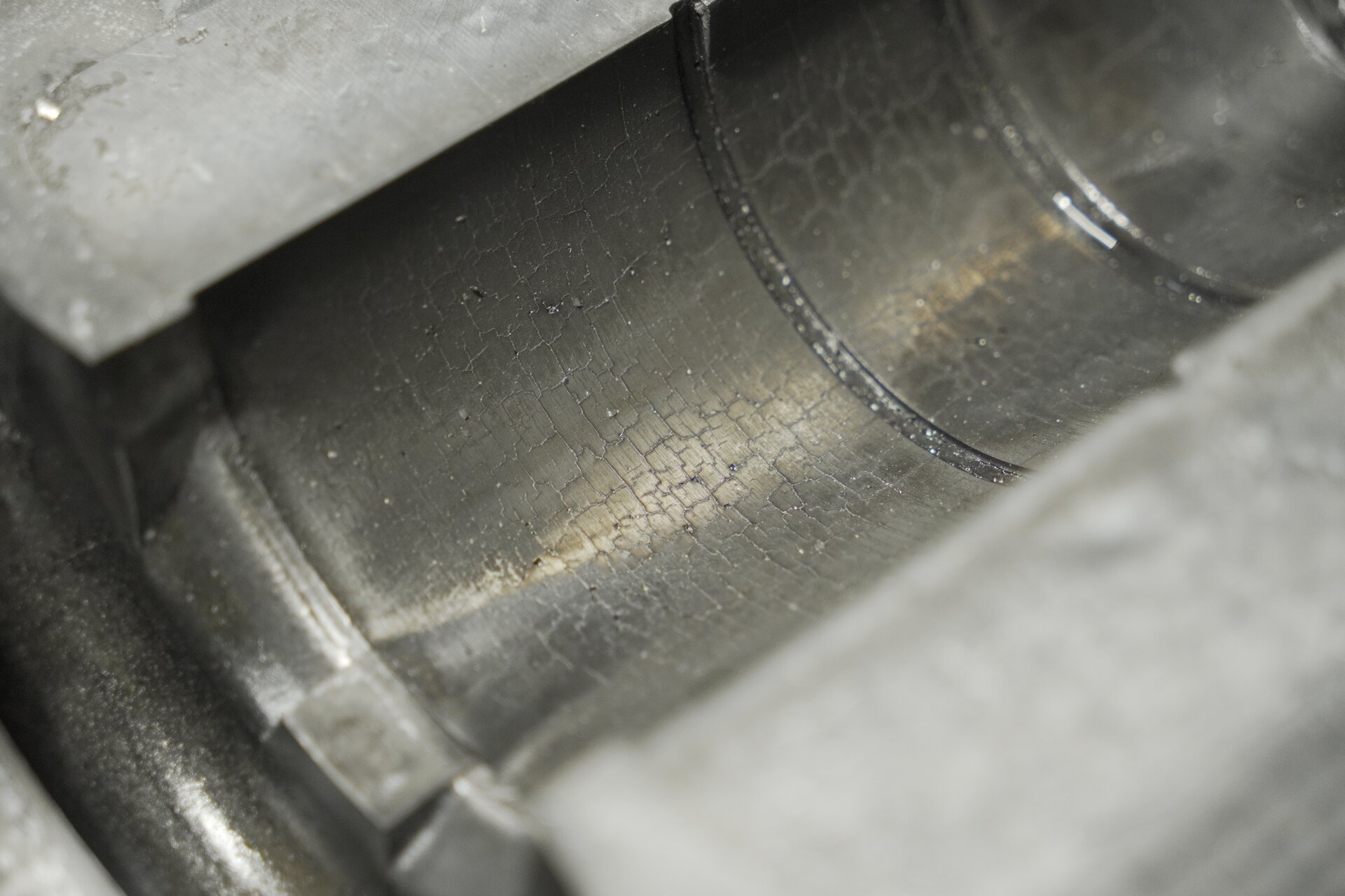 Ilustracja przedstawia zużyta formę metalową. Widoczna jest wnęka formy, z popękaną powierzchnią w kształcie siatki.