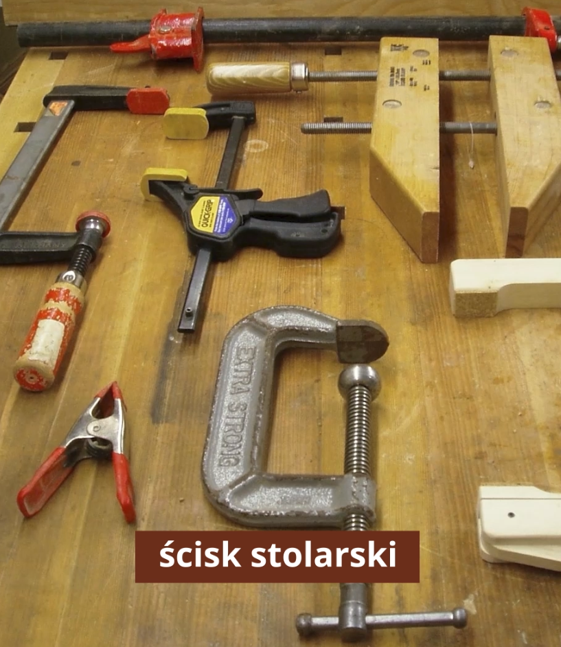 Zdjęcie przedstawia ściski stolarskie. Są to narzędzia składające się z dwóch elementów. Jeden element ma kształt litery C. Na końcu jednego ramienia znajduje się otwór, w który wkręcany jest drugi prosty element, służący do ściskania. Koniec drugiego ramienia jest płaski.