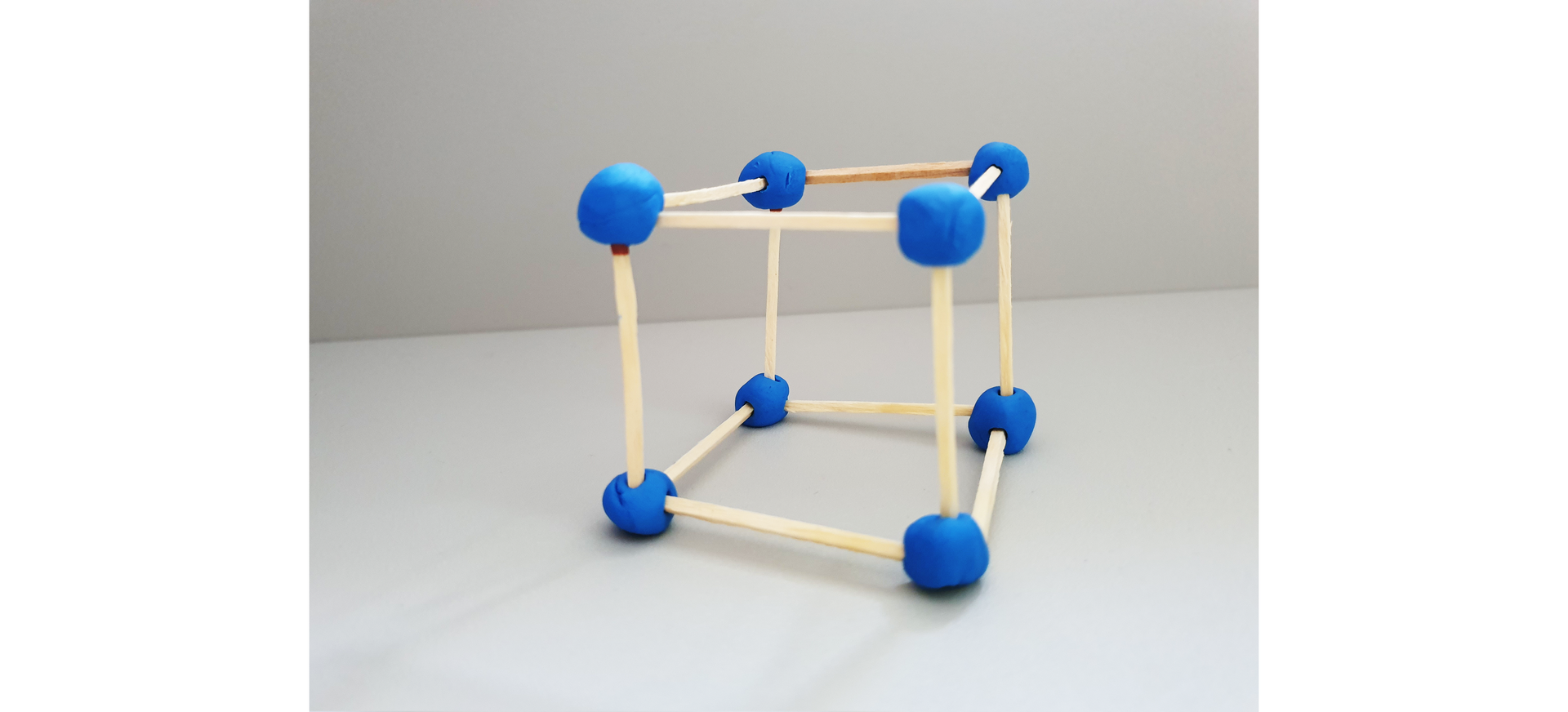 Ilustracja przedstawia szkielet sześcianu, którego krawędziami są drewniane wykałaczki, a wierzchołkami kulki z plasteliny umożliwiające łączenie krawędzi.