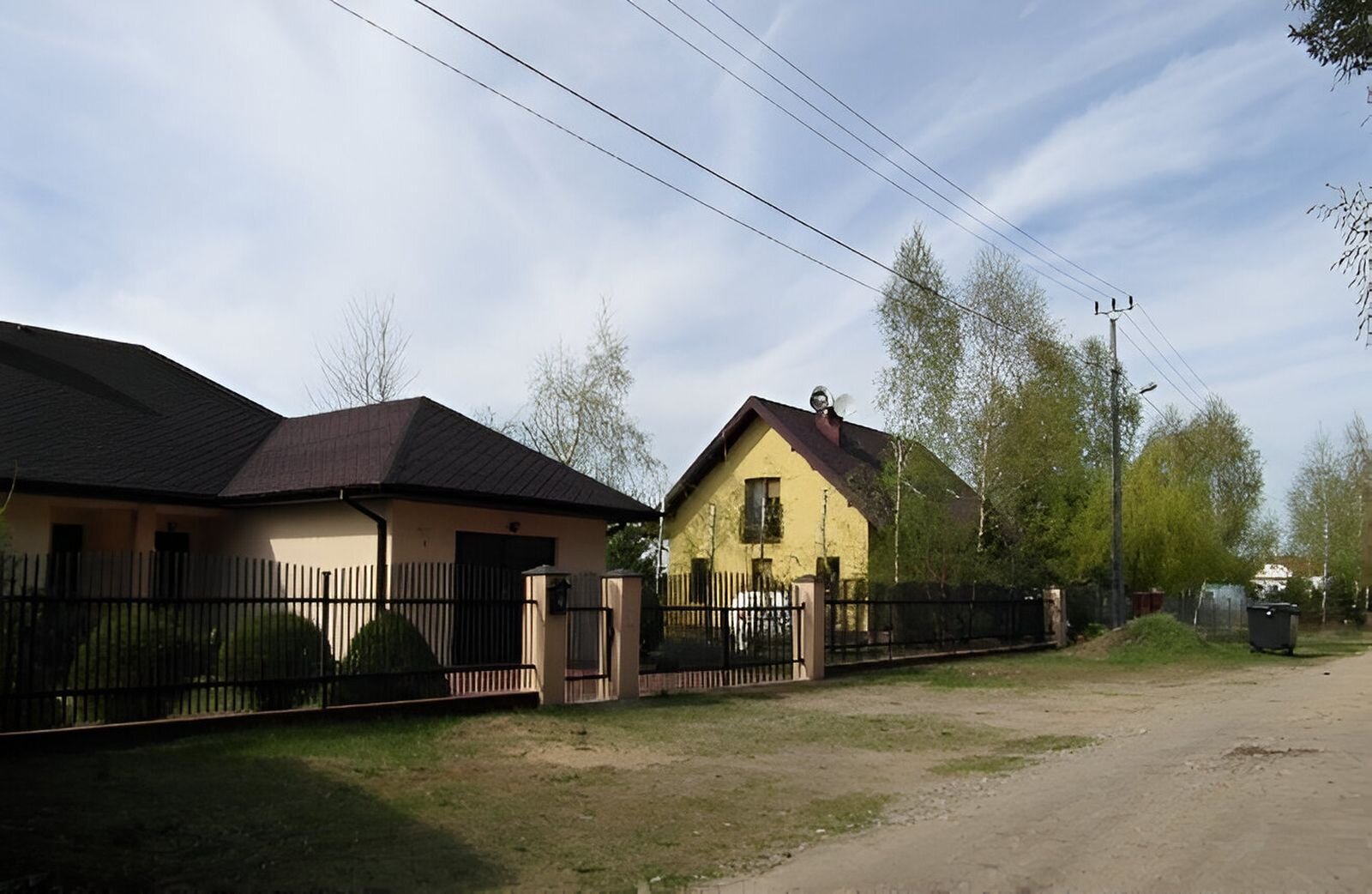 Fotografia przedstawia dwa domy, pierwszy z brzegu ma beżową elewację i brązowy dach, drugi żółtą elewację i ciemny dach. 