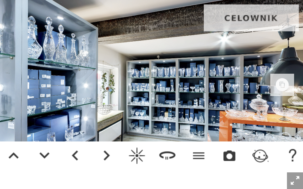 Zdjęcie przedstawia ekran startowy wycieczki wirtualnej. Znajduje się tu zdjęcie sklepu z ekspozycją szkła kryształowego. Pod zdjęciem znajduje się pasek nawigacji i przyciski umożliwiające nawigowanie do góry, w dół, w lewo i prawo, przycisk ukryj hotspoty, włącz autonarrację, otwórz / zamknij menu boczne, zrób zdjęcie, pokaż widok „mała planeta”, pokaż ekran pomocy, ukryj nawigację.