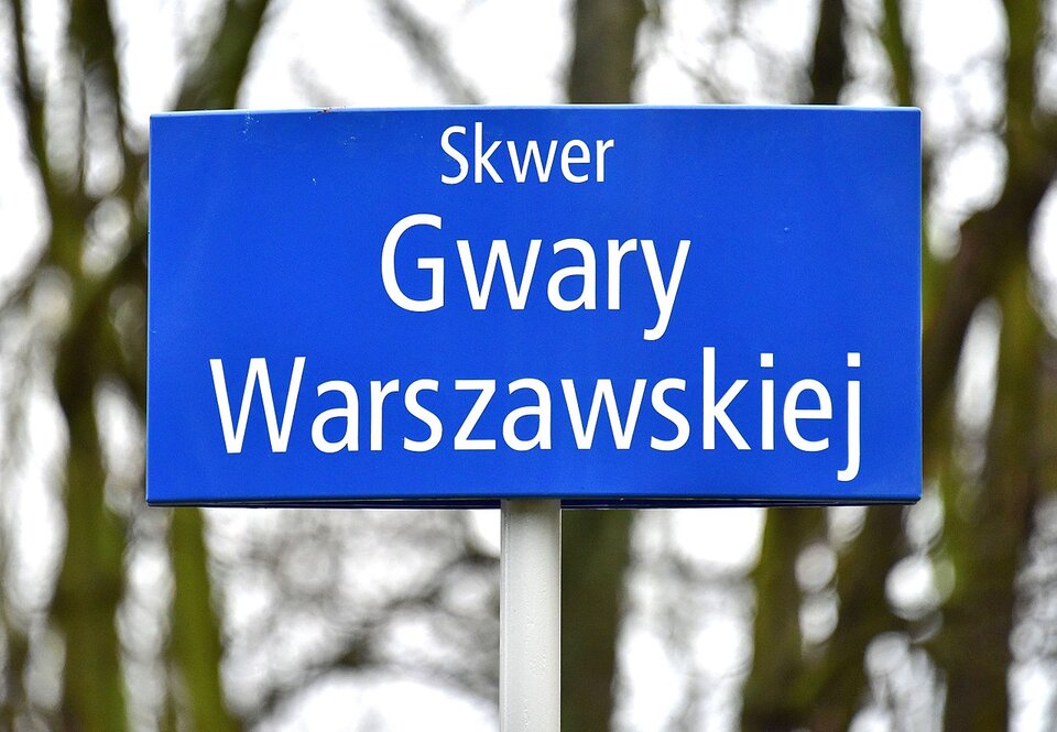 Zdjęcie przedstwia znak informacyjny. Na niebieskiej tabliczce widnieje napis: "Skwer Gwary Warszawskiej".