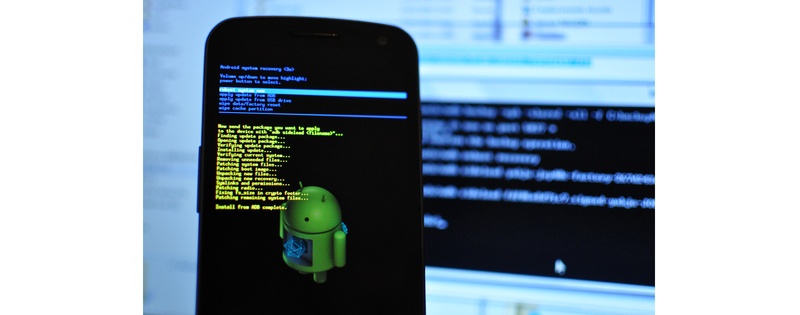 Zjęcie przedstawia telefon komórkowy z sytemem Adroid uruchomiony w trybie Recovery. Na ekranie widoczne są nieczytelne napisy i logo Androida - zielony robot.